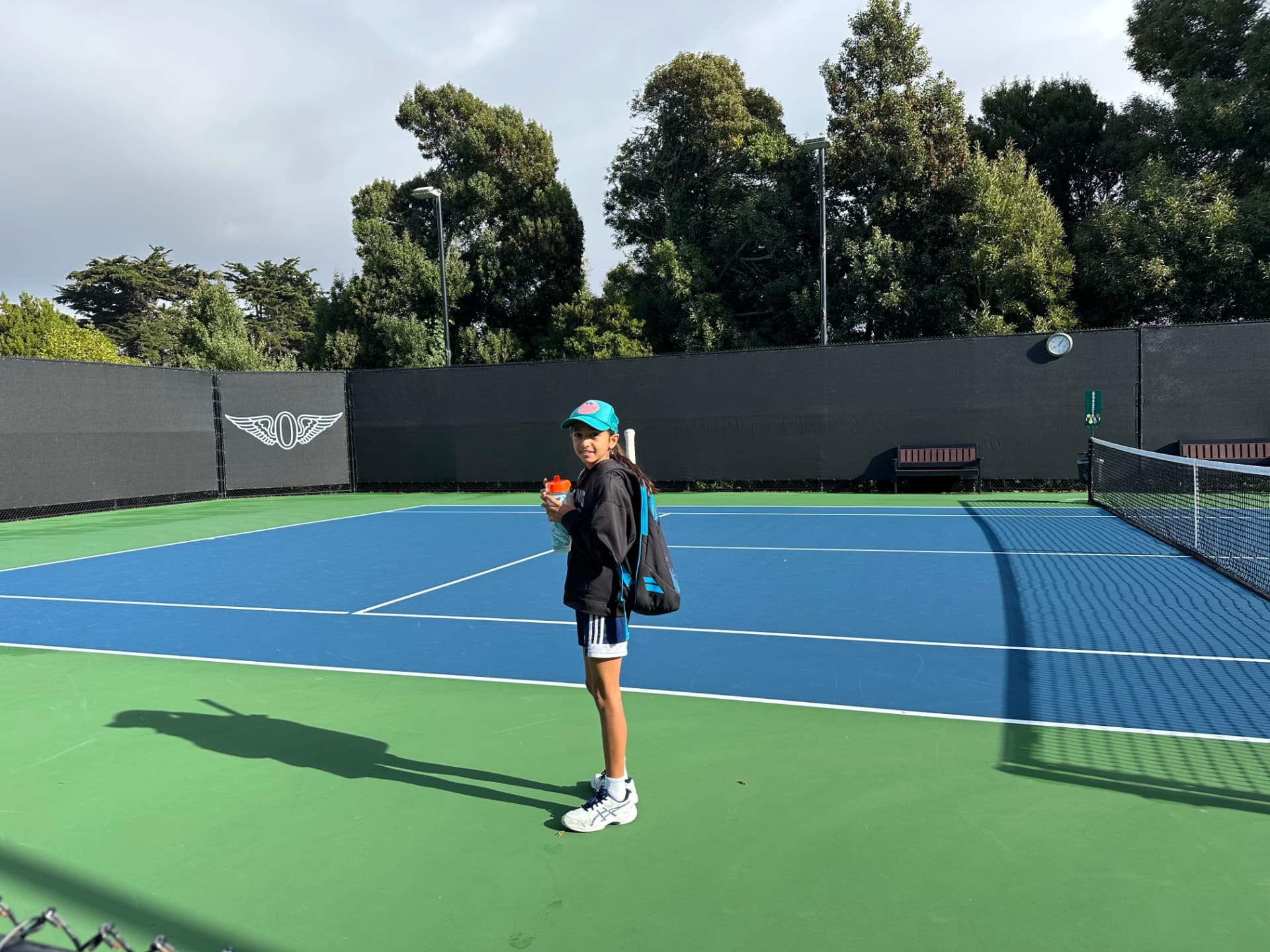 Noor standing on a tennis court with her bag and water bottle