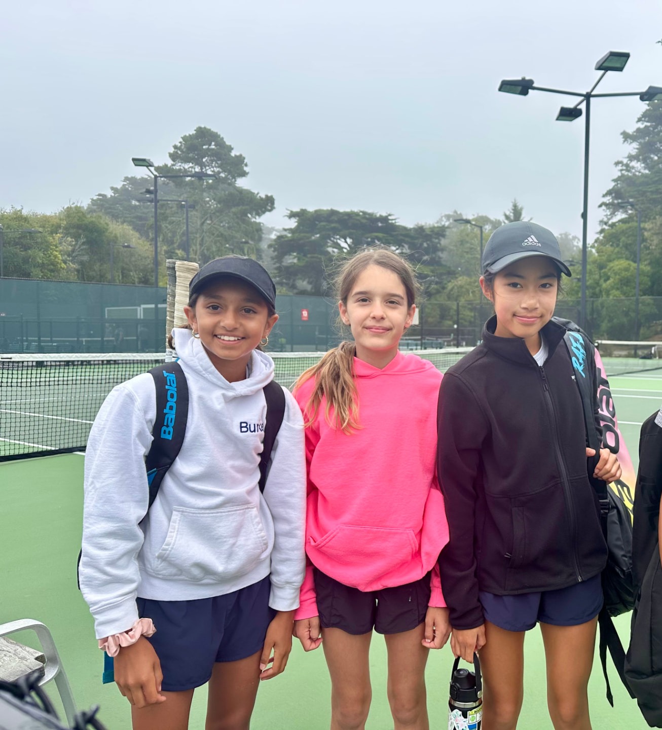 Three young tennis players standing together on a green tennis court